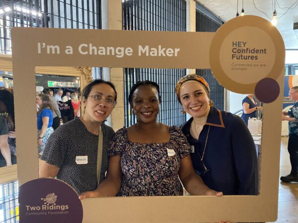 Three smiling women holding a cardboard frame that was "I am a changemaker"
