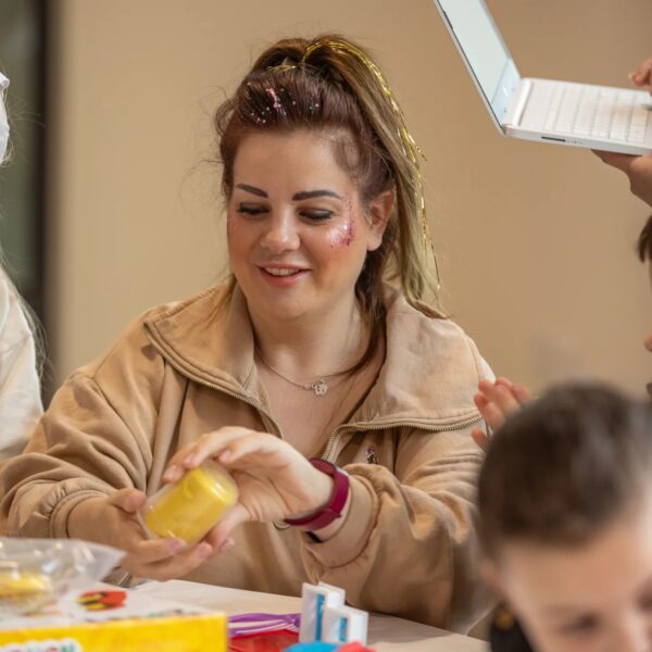 Woman smiling while doing crafts at a table. She has glitter on her face.