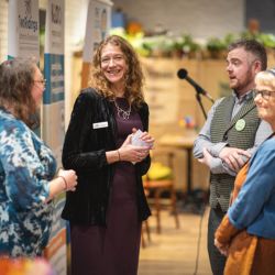 Four people chatting at an event. The lady in the centre is looking straight at the camera.
