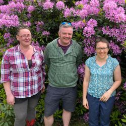 Three people stood in front of a purple flower 