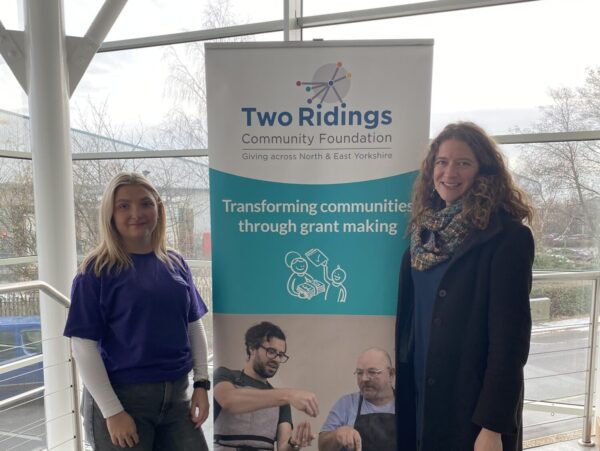 Two women stood in front of a banner smiling