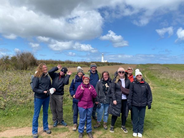 Group of nine people standing on a grassy path. Everyone is posed facing the camera, appearing relaxed and cheerful.
