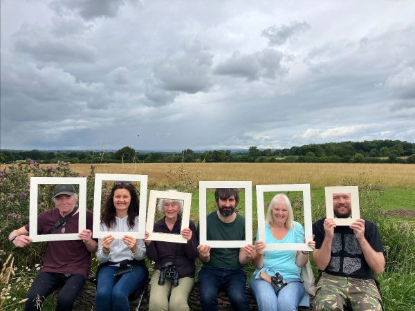Poeple sta in front of a field with frames around six faces
